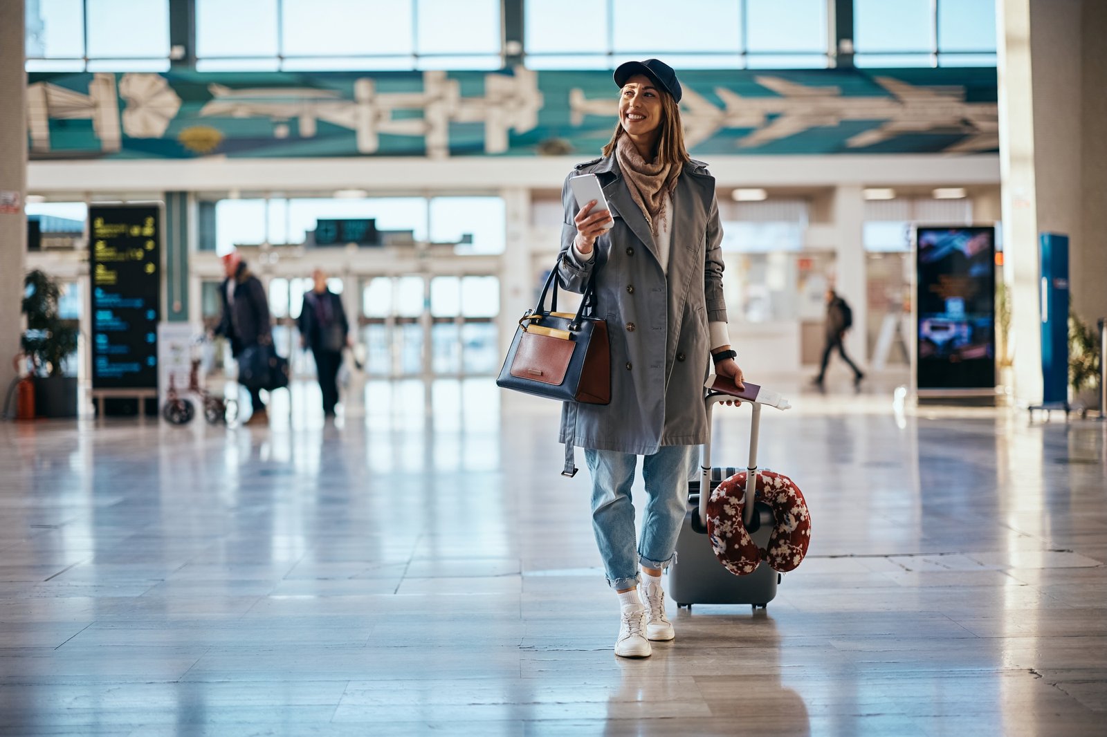 Young happy traveler with her suitcase walking through airport terminal.